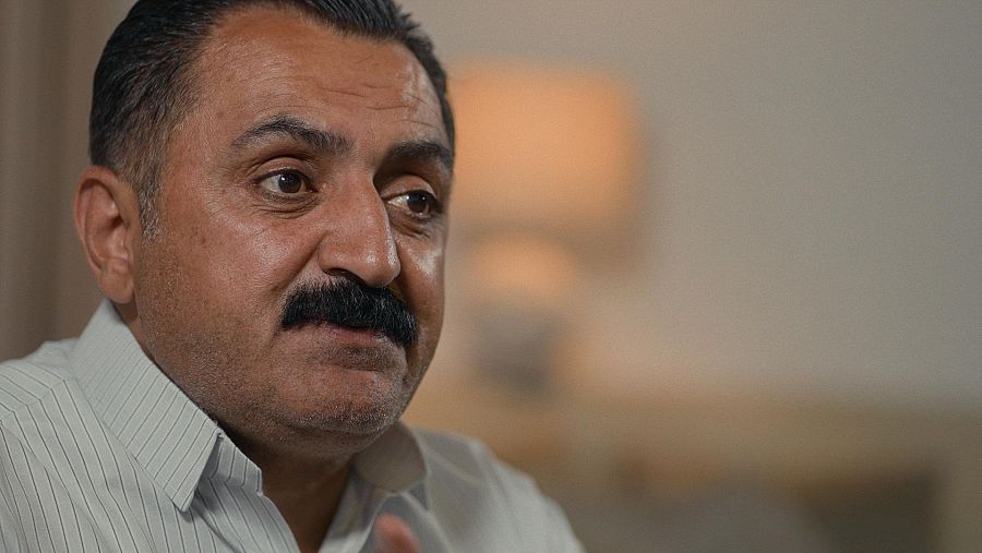 Retrato de un médico de mediana edad con cabello y bigote oscuros, tez morena y camisa clara a rayas.  Su expresión denota concentración.