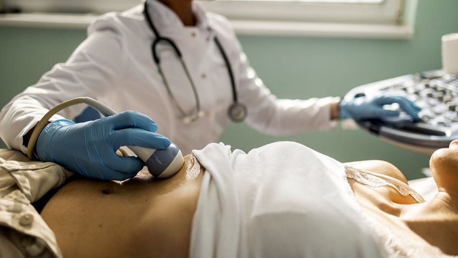 Ecografía abdominal: Doctora con bata blanca y guantes azules realiza un examen a una paciente en camilla.