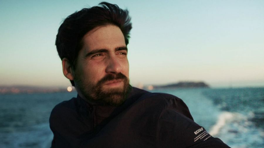 Javier Peña, en una embarcación, observa el mar al atardecer.  Viste chaqueta oscura con la etiqueta 'ECOALF' visible.  Imagen promocional del documental 'HOPE'.
