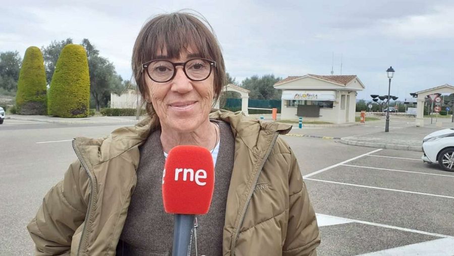 Entrevista a la gestora de Panorámica en la entrada de la urbanización.  Se la ve con un micrófono, gafas y chaqueta beige, frente a una caseta de seguridad.