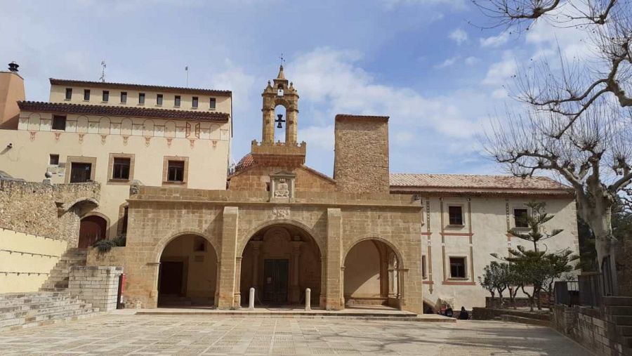 Fachada de piedra con tres arcos, campanario cuadrado con reloj y cruz, y torre adyacente en el Real Santuario Font de la Salut.