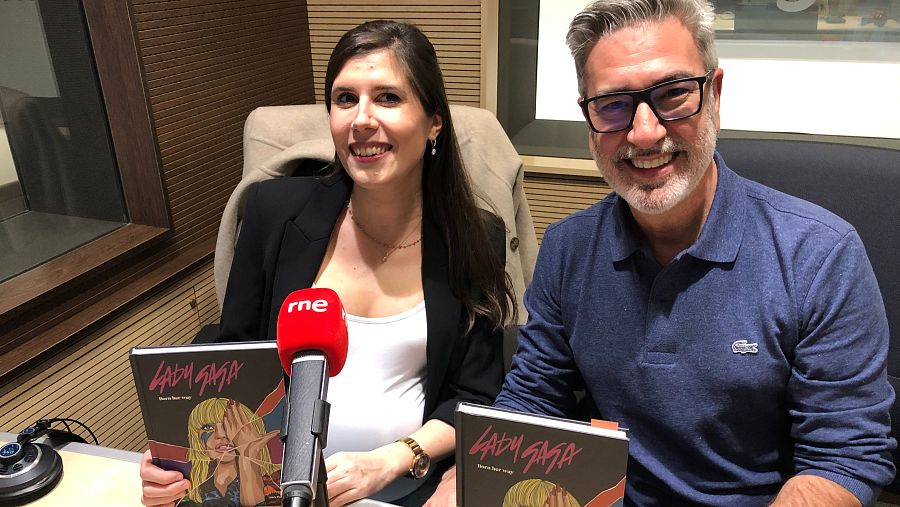 Dos personas sonríen a cámara en un estudio de radio, sosteniendo un libro con la portada de Lady Gaga. Un micrófono con el logo de RNE está entre ellos.