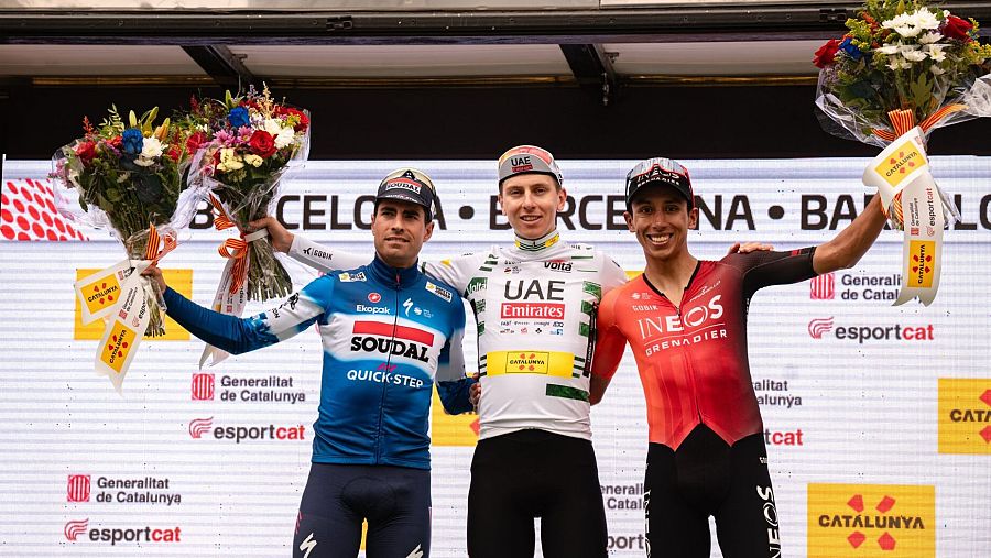 Podio de la Volta Ciclista a Catalunya 2025: tres ciclistas con maillots de diferentes equipos, sosteniendo flores, frente a un cartel con el nombre de Barcelona.