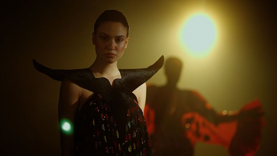 Modelo con vestido oscuro y alas, detalles brillantes, iluminación dramática; fotograma de documental sobre Paco Rabanne.