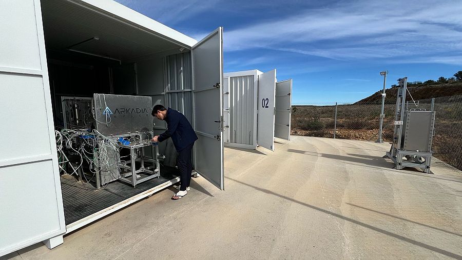 En las instalaciones de Arkadia Space, un hombre trabaja en equipos dentro de un contenedor blanco abierto, junto a otro contenedor marcado con '02'.