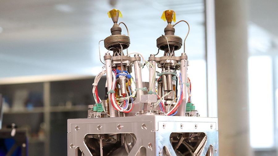 Dos motores cilíndricos con conexiones de cables y tubos sobre estructura metálica cuadrada.  Piezas ámbar en la parte superior de los motores.