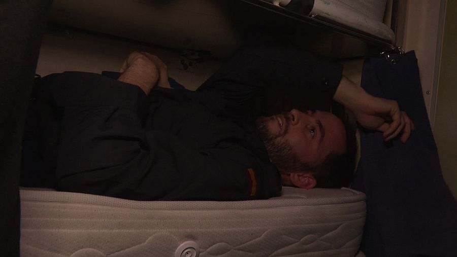 Tripulante en litera de submarino, uniforme oscuro con insignia. Espacio reducido, camas aprovechadas al máximo.