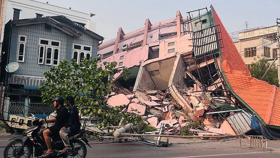Dos personas pasan en moto por delante de un edificio derrumbado en Mandalay