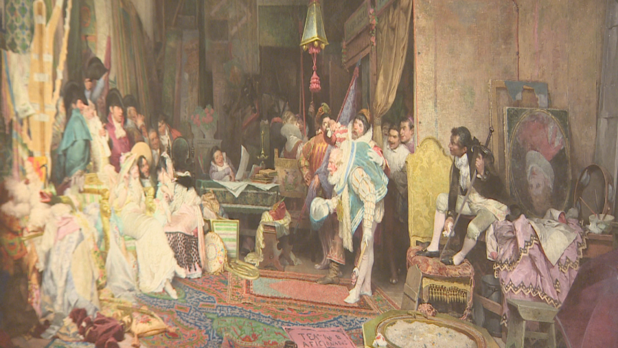 Escena teatral cortesana del siglo XIX: un bufón en traje azul y blanco es el foco de atención de un grupo en un interior con piano y otros objetos.  Detalles de vestuario y ambientación.