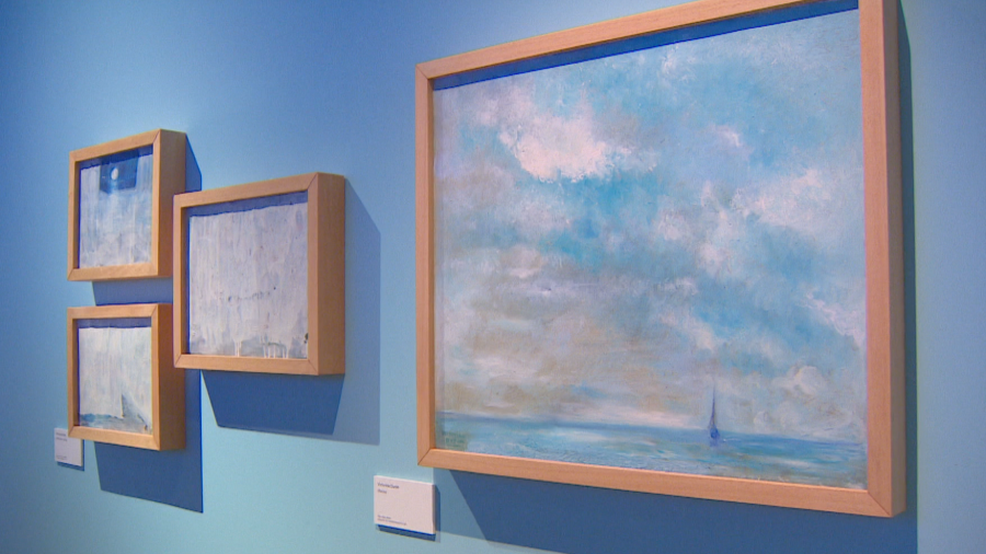 Cuatro óleos con marcos claros, tres pequeños (abstractos o marinos) y uno grande (paisaje marino), expuestos en una sala con paredes azules.