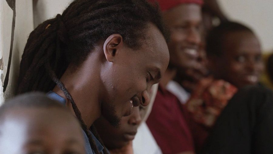 Hombre con rastas sonriendo rodeado de niños, mostrando alegría y conexión en un ambiente interior positivo.