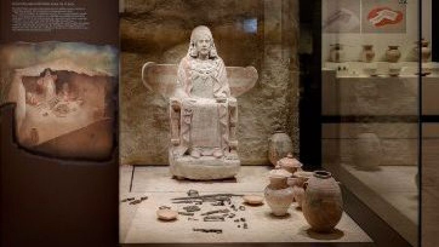 Escultura de la Dama de Baza en vitrina museística, acompañada de objetos y paneles informativos sobre su descubrimiento e historia.