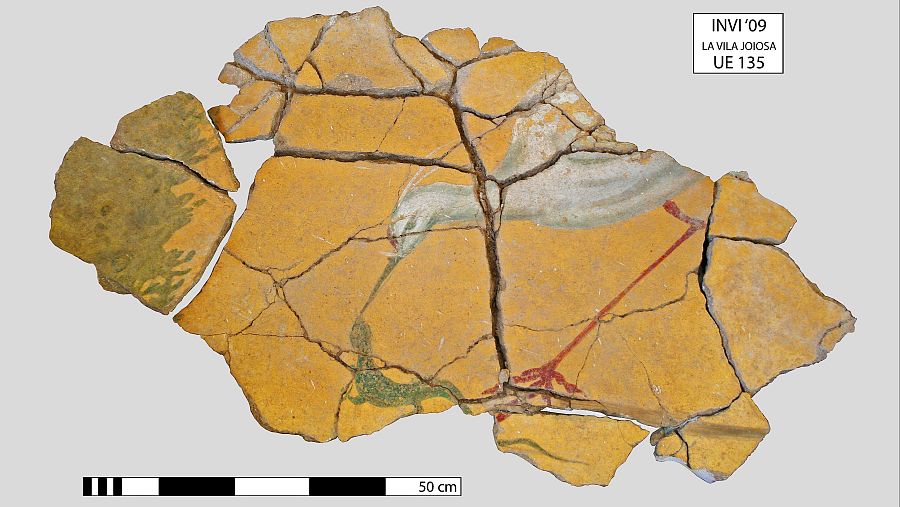 Panel mural en restauración con escena natural: ave blanca, reptil verde y vegetación sobre fondo ocre agrietado.  Marcas de inventario y escala (50cm aprox.).