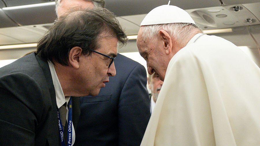 El Papa Francisco y un periodista conversan a bordo de un avión. El periodista porta una acreditación 'Press Office'.