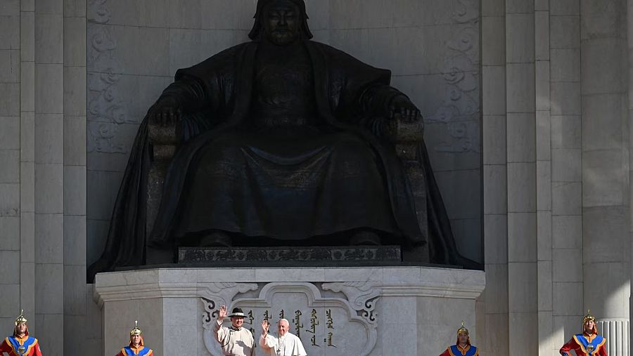 El Papa Francisco y un acompañante saludan una gran estatua de Gengis Kan, custodiada por guardias en vestimenta tradicional mongola.