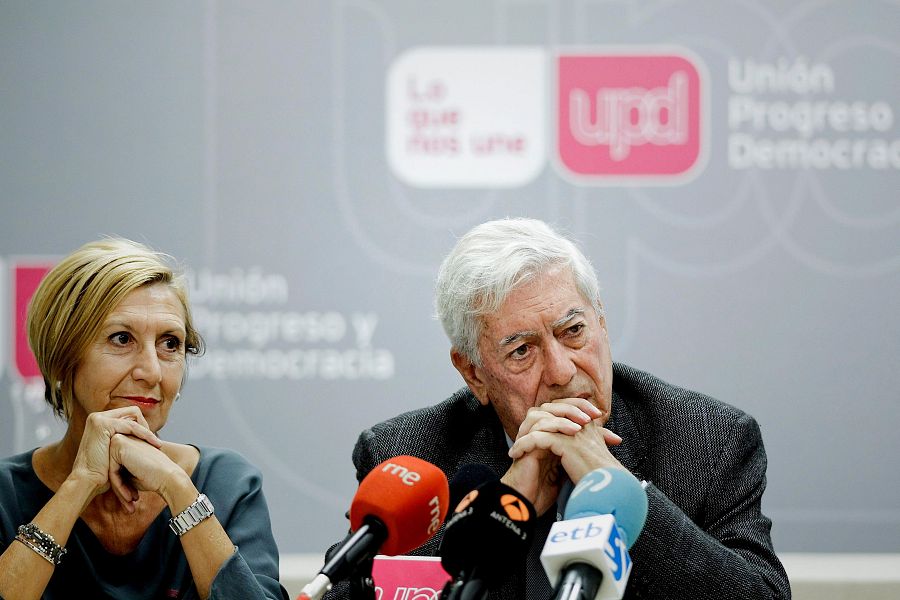 Rosa Díez y Mario Vargas Llosa, sentados en un desayuno de prensa, con micrófonos de medios presentes y el logo de UPyD visible al fondo.