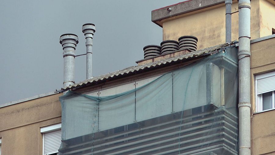 Parte superior de un edificio con chimeneas metálicas, estructuras de ventilación, una galería cubierta con malla verde y ventanas con persianas.