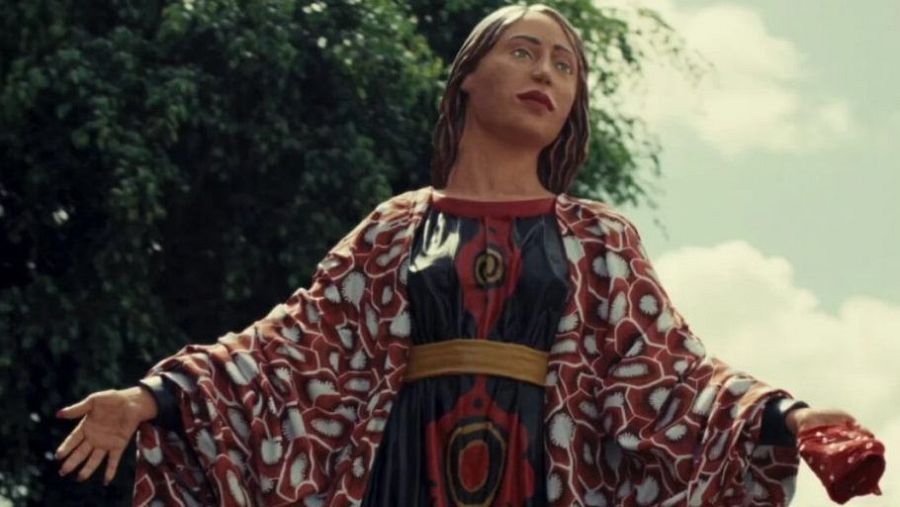 Estatua al aire libre representando a un personaje femenino con vestido oscuro y chal con estampado rojizo y blanco.  Postura acogedora, escena de homenaje.