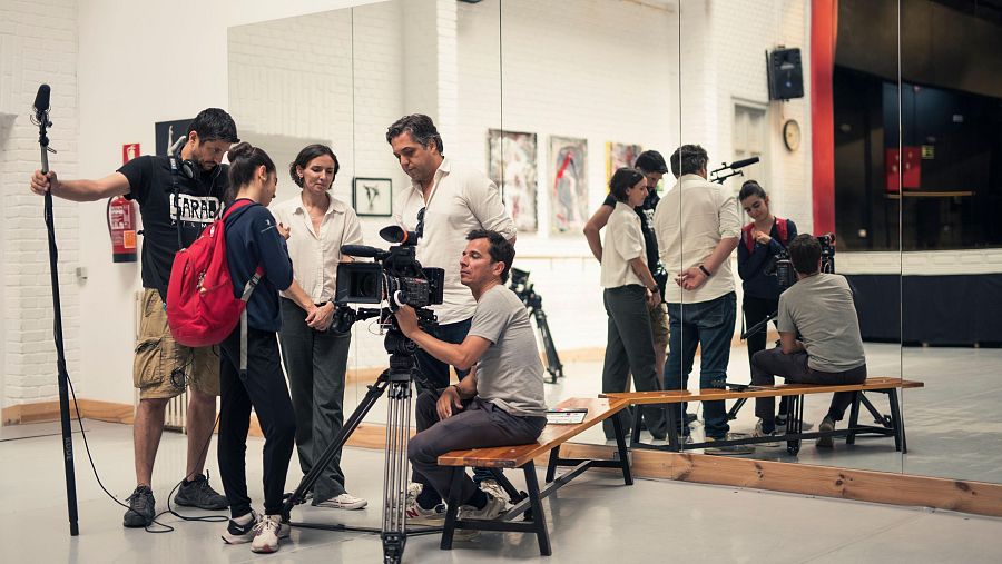 Equipo de rodaje documentando una entrevista o ensayo en un estudio. Se observa un camarógrafo, sonidista y varias personas del equipo de producción.