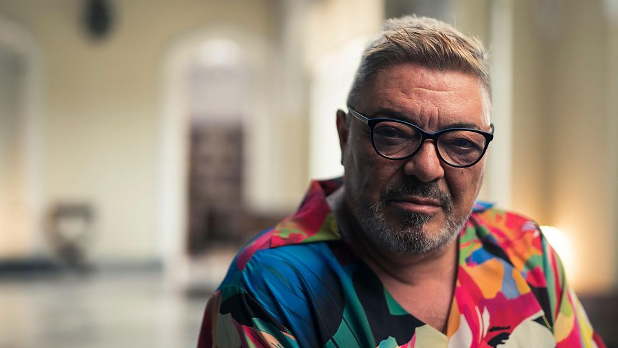Retrato de Antonio Canales: hombre de mediana edad con camisa floral, gafas y expresión seria. Fondo interior difuminado.