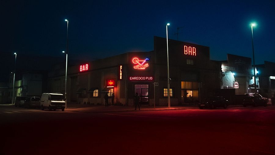 Calle nocturna con bares y restaurantes; letreros luminosos de 