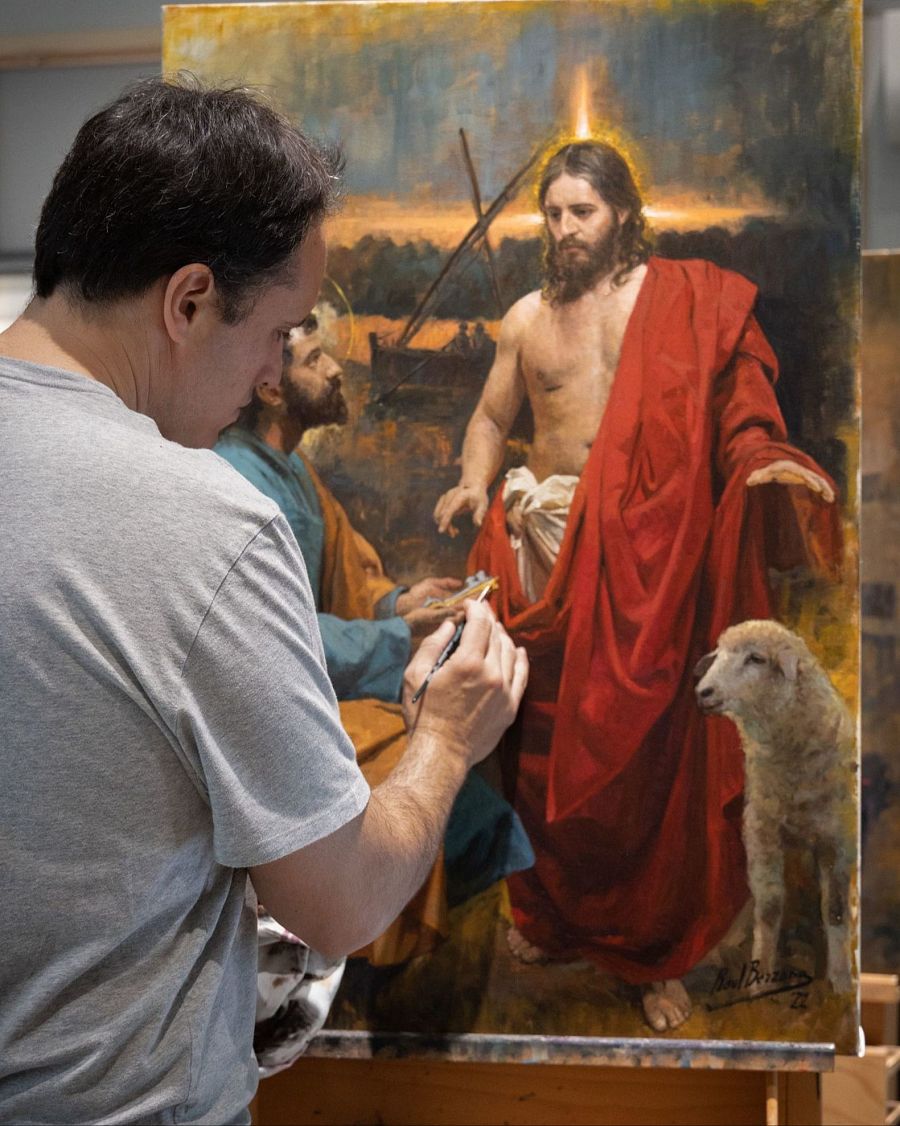 Raúl Berzosa pinta un cuadro religioso mostrando a Jesús con túnica roja, un cordero y un apóstol; la escena está iluminada con luz cálida.