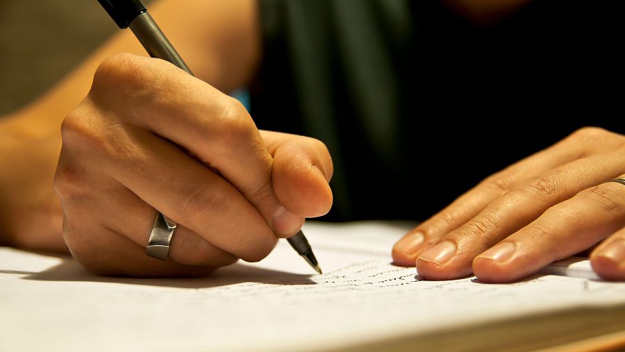 Sobre un cuaderno, una persona escribe unas palabras