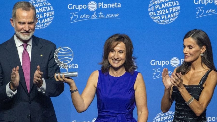 Entrega del Premio Planeta: la ganadora, con el trofeo, es felicitada por los Reyes de España.  Fondo con logo del Grupo Planeta y '75 años'.