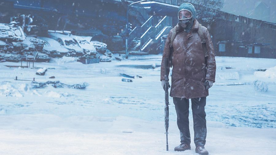 Figura solitaria con rifle y máscara antigás en paisaje nevado, vehículos y edificios cubiertos de nieve al fondo. Ambiente postapocalíptico.