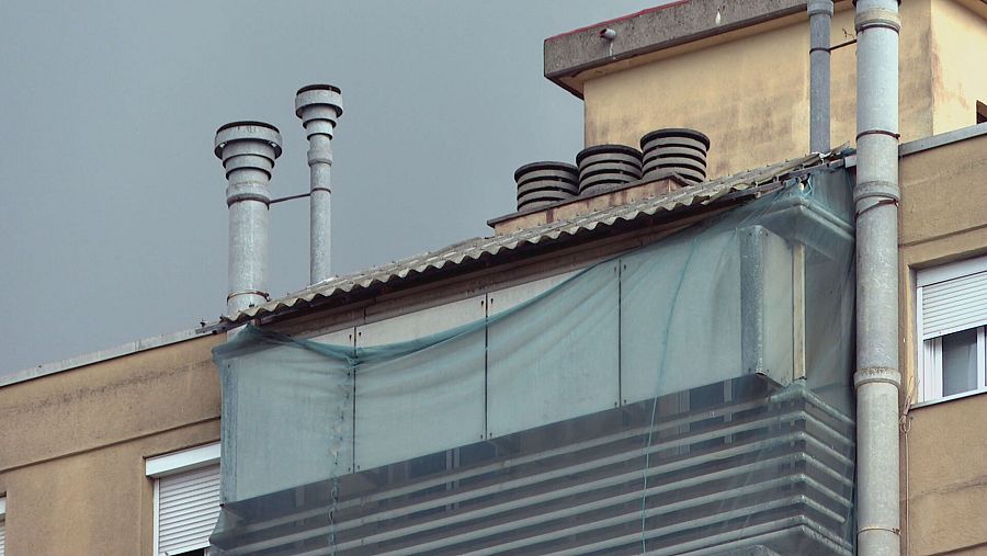Azotea con dos chimeneas metálicas, varias ventilaciones cilíndricas y una estructura con malla protectora verde azulada. Fachada beige y cielo gris.