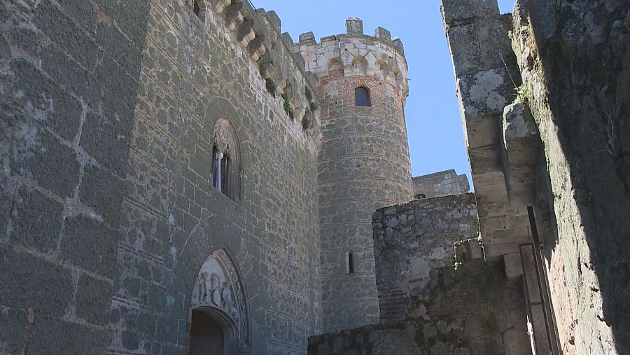 Torre cilíndrica almenada y muro de piedra con ventanas, mostrando detalles arquitectónicos en un acceso a la zona palaciega de un castillo.