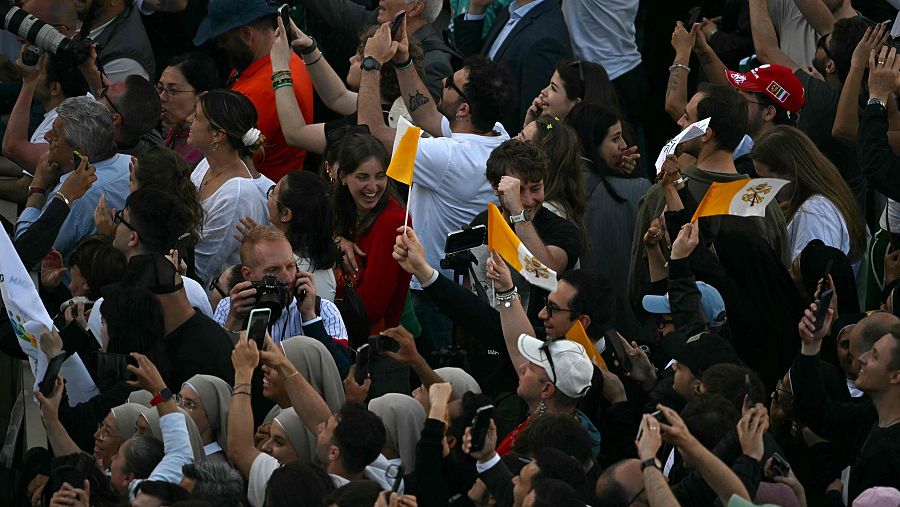 La gente reacciona y agita banderas vaticanas cuando se ve la fumata blanca