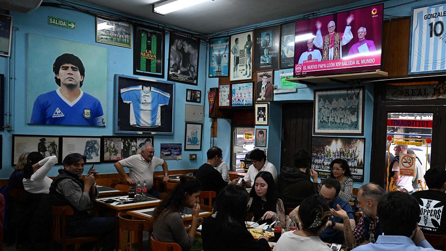 El Papa León XIV aparece en un televisor mientras la gente come en un restaurante de Buenos Aires