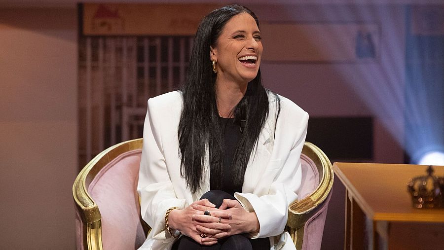 María Silóe sonríe en un sillón rosa con detalles dorados, durante la grabación de 