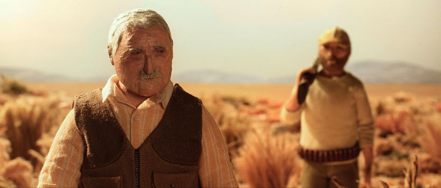 Primer plano de un hombre mayor serio, con camisa a rayas y chaleco, junto a otro con barba y gorra, portando un rifle.  Ambientación desértica, técnica stop-motion.