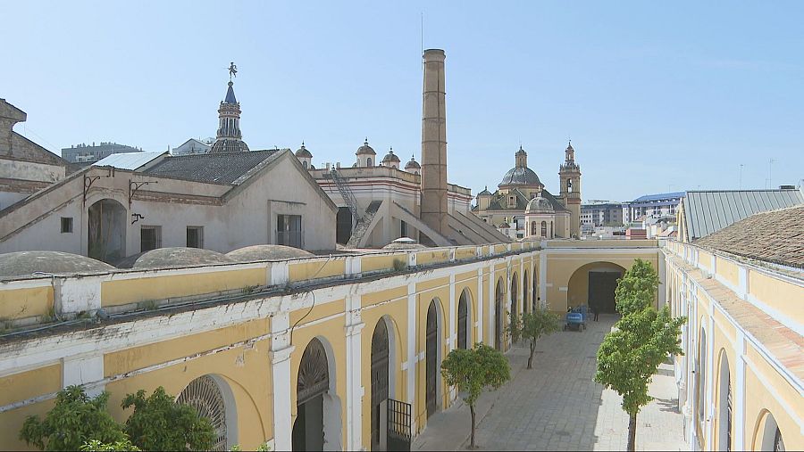 Patio interior de edificio amarillo con arcos, cúpulas y árboles.  Se aprecia un vehículo aparcado al fondo.