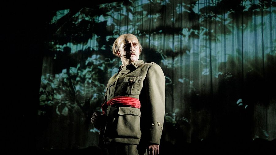 Juan Vinuesa, en uniforme militar verde oliva y faja roja, interpreta a Francisco Franco en la obra '1936'. Mira fijamente a la cámara.