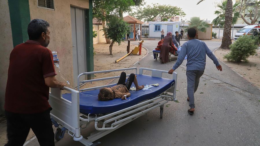 Evacuación de pacientes en camillas tras ataques aéreos. Un niño recibe tratamiento intravenoso mientras lo trasladan.  El caos y la urgencia se reflejan en la imagen.