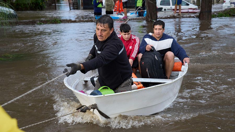 Un hombre tira de una cuerda para deslizar un bote que transporta residentes a través de una calle inundada tras fuertes lluvias en Campana, Argentina