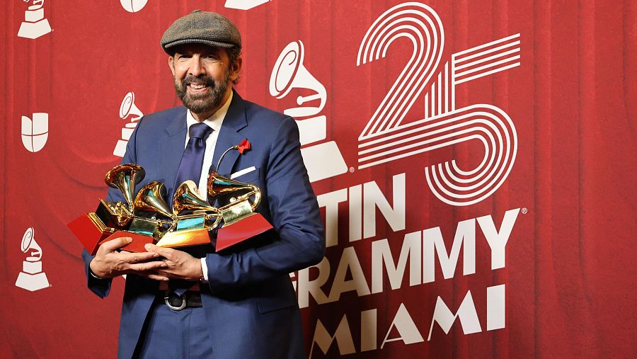 Cantante con varios premios Grammy, traje azul oscuro, camisa clara, boina gris y sonrisa. Fondo rojo con logo de los Latin Grammy y el número 25.