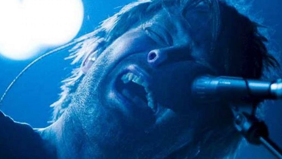 Primer plano de Thom Yorke cantando con un micrófono, iluminado con una intensa luz azul en un concierto.