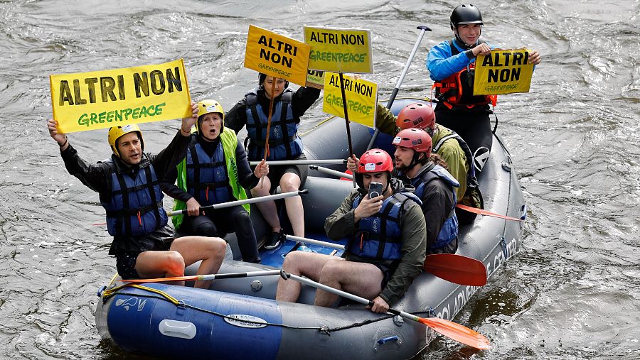 Protesta en balsa fluvial: siete personas con chalecos y cascos, portando pancartas con lemas visibles, participan en una manifestación.