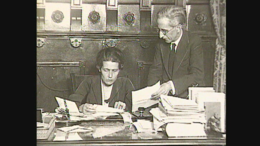 Abogada revisando papeles en un escritorio junto a un hombre; imagen en blanco y negro que sugiere intensa actividad laboral en una oficina.