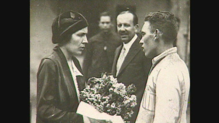 Victoria Kent, en visita a una prisión, conversa con un hombre mientras otro la observa.  Un ramo de flores está presente en la imagen en blanco y negro.
