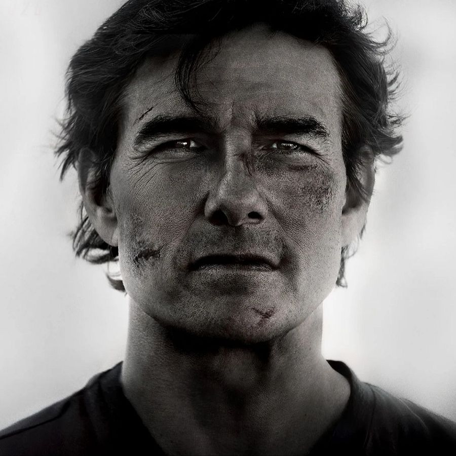 Tom Cruise, rostro magullado y sucio, mirada seria, cicatrices en mejilla y labio.  Imagen en blanco y negro, camiseta oscura.
