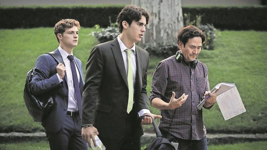 Tres hombres, dos en traje y uno con camisa a cuadros sosteniendo un guion, posiblemente durante el rodaje de una película.