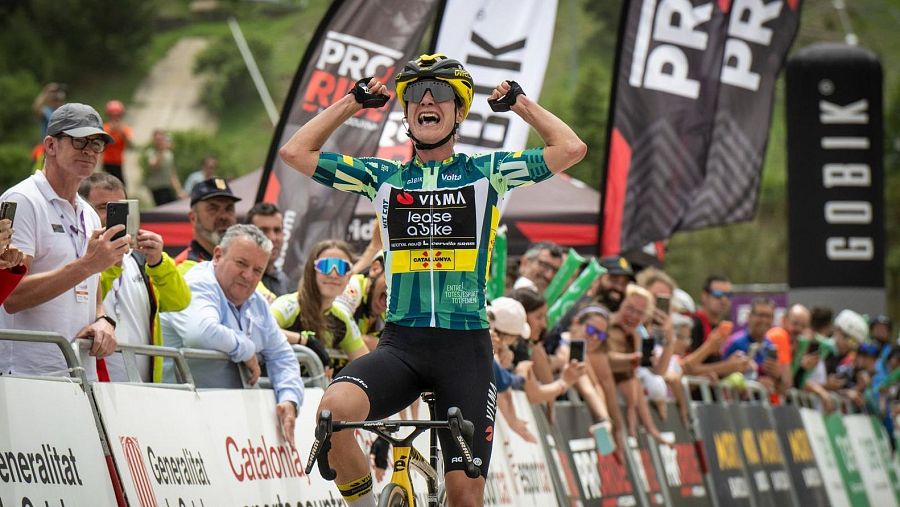 Ciclista celebrando una victoria en meta, con multitud de espectadores y vallas publicitarias visibles.