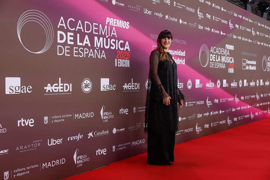 Rozalén posa en la alfombra roja de los Premios de la Academia de la Música de España.  Viste un largo vestido negro con flecos y el photocall muestra logos de patrocinadores.