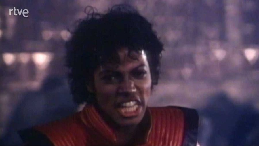 Primer plano de Michael Jackson con expresión seria, chaqueta roja con hombreras, fondo oscuro y borroso.  Imagen que sugiere una referencia a su pasado.