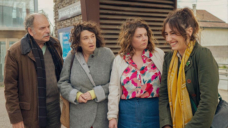 Cuatro personas conversan en una calle junto a un edificio con la inscripción 